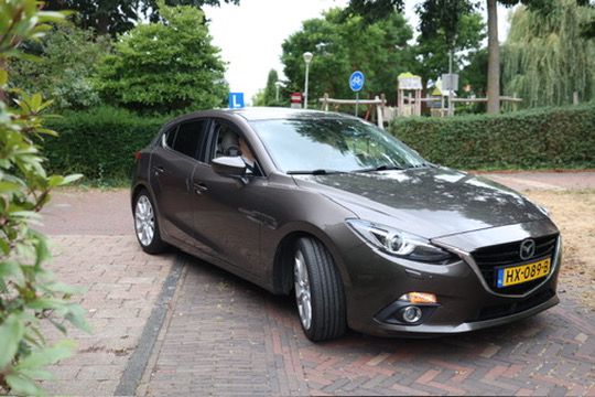 De bruine Mazda 3 lesauto van Nova Drive met L-bordje op het dak