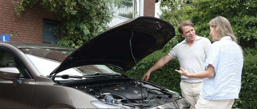Slava legt onder de geopende motorkap de techniek van de lesauto uit aan een leerling